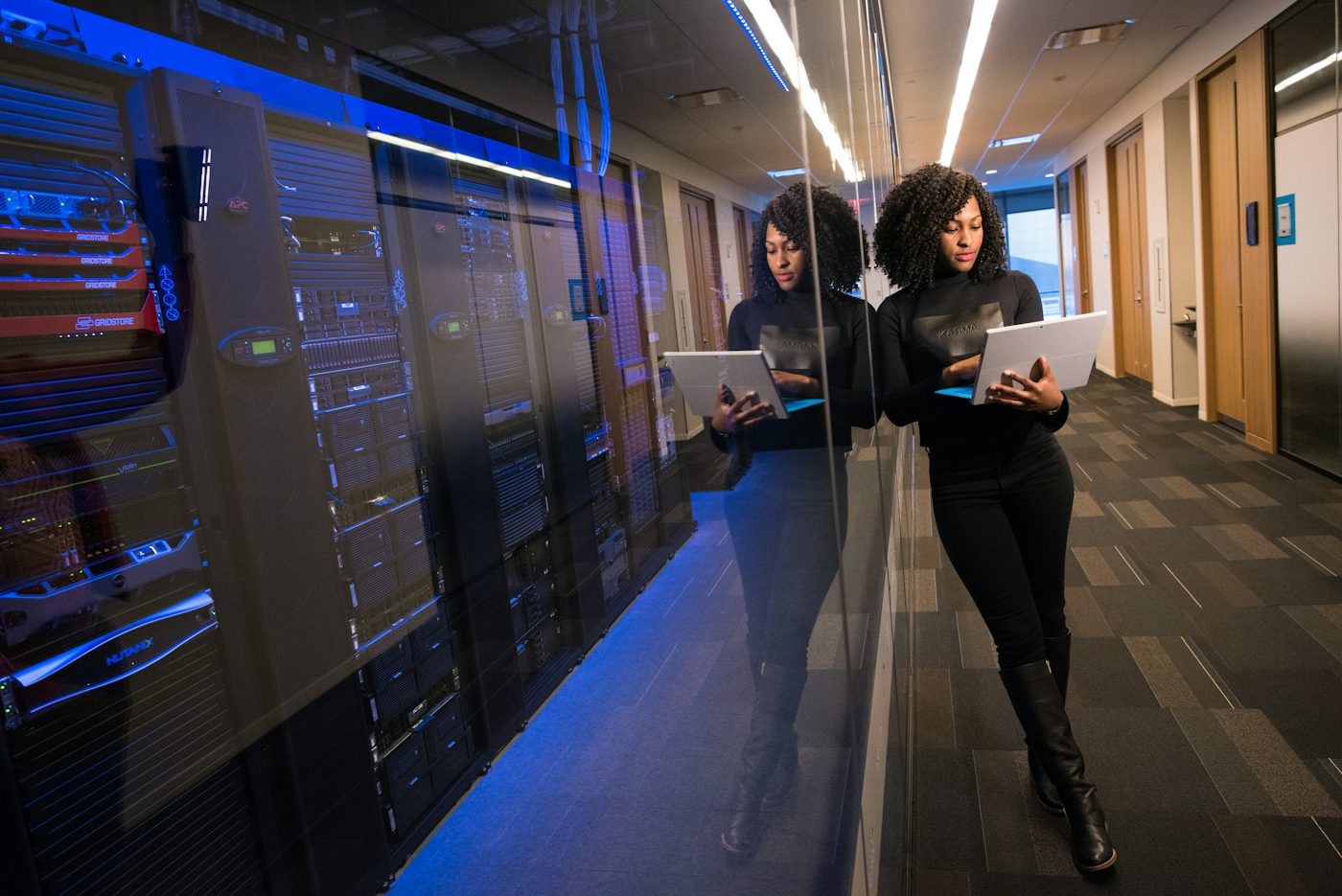 Two colleagues walking with laptops past a lit corridor at night.